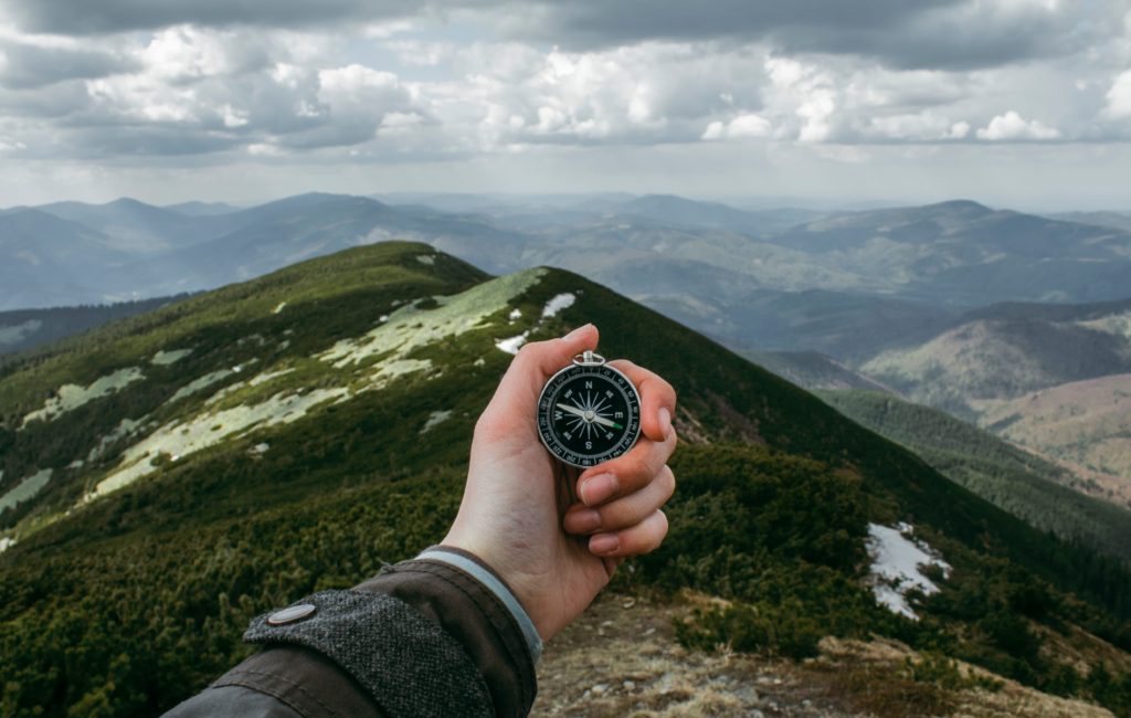 person holding compass on a mountain side